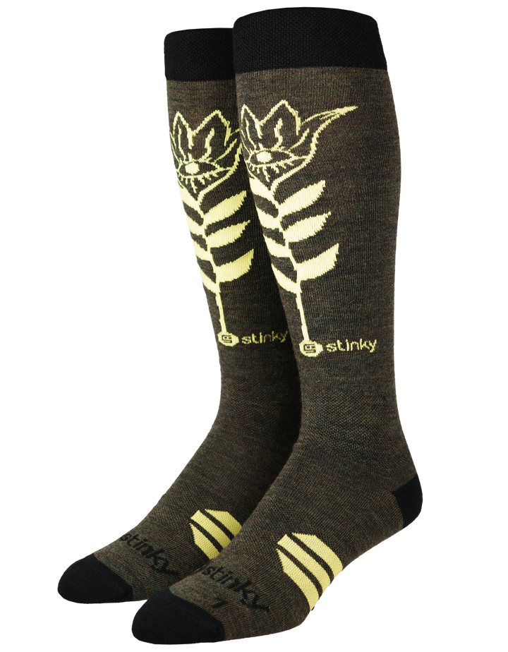 A pair of dark olive brown knee-high socks with a cream-colored stylized fern leaf graphic and the brand name 'stinky' printed near the calf, shown on a plain white background.